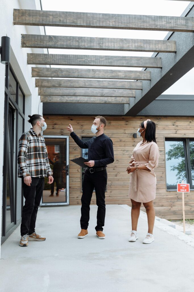 pexels-photo-8482553-8482553 A real estate agent shows a house to clients while wearing face masks for safety.